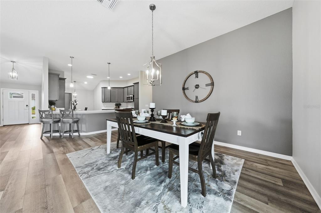 A dining area with a wooden table, chairs, and a large wall clock on gray walls — 2006 OPPENHEIMER COURT, THE VILLAGES, FL