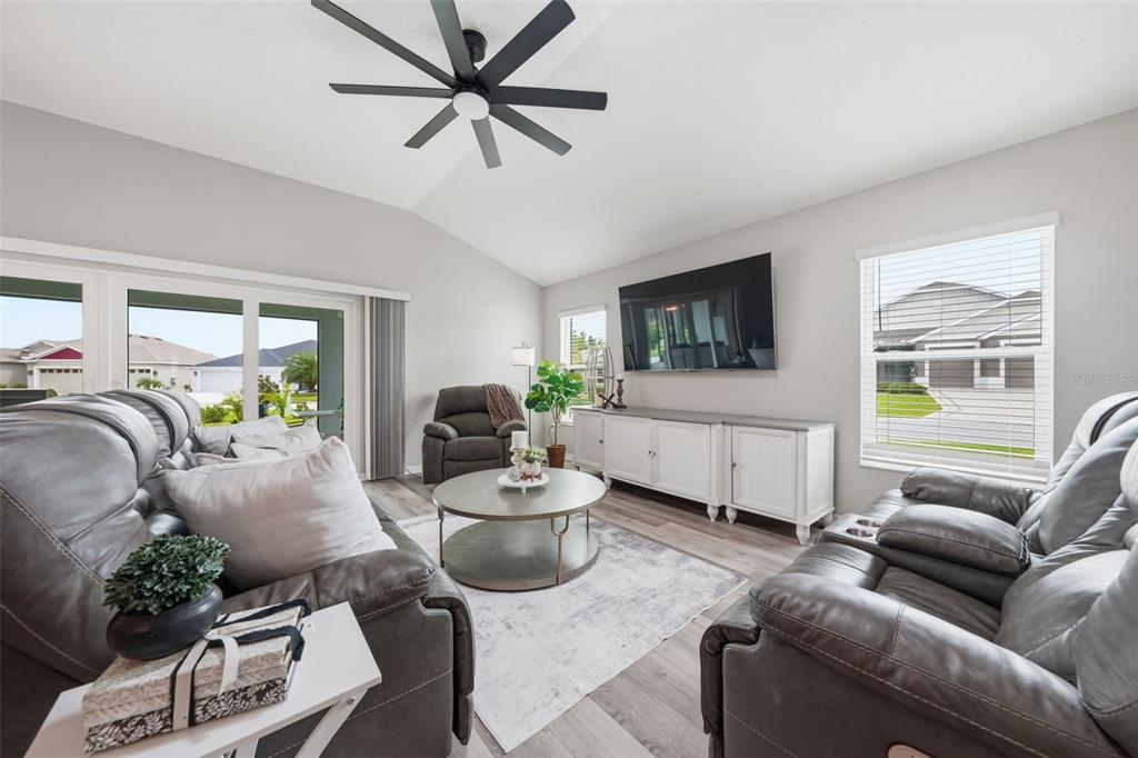 A living room features gray leather furniture, a round coffee table, and a wall-mounted television — 2006 OPPENHEIMER COURT, THE VILLAGES, FL