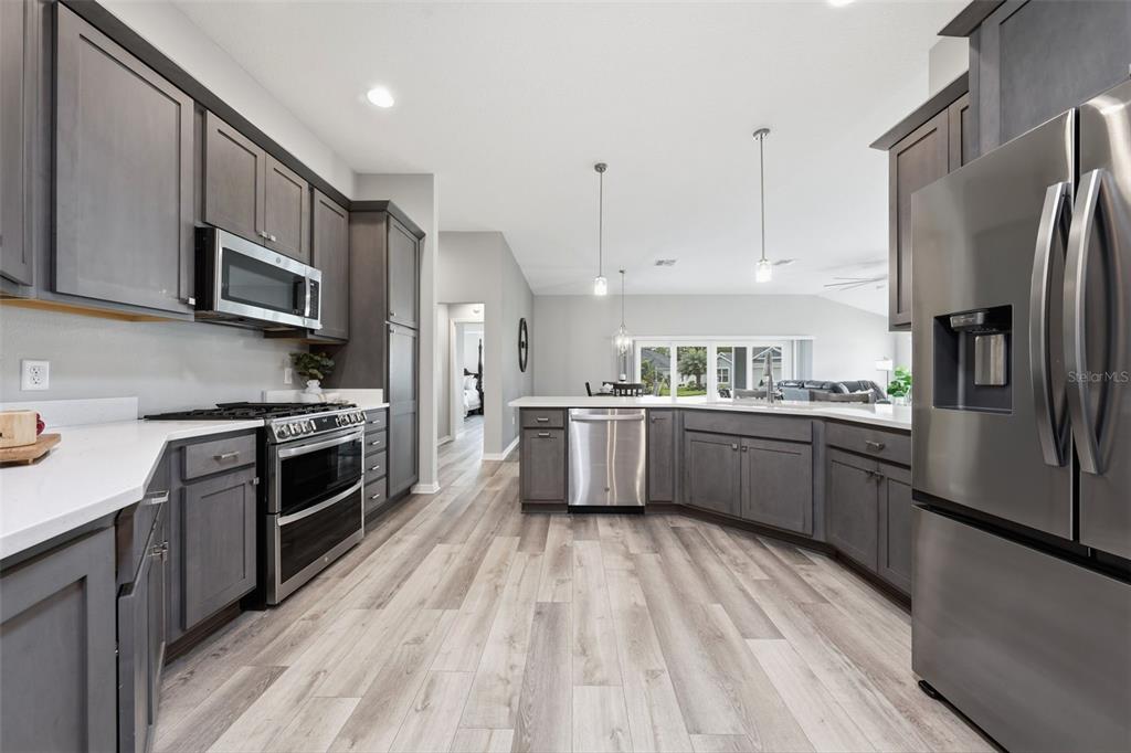 A modern kitchen features dark gray cabinetry, stainless steel appliances, and light wood-look flooring — 2006 OPPENHEIMER COURT, THE VILLAGES, FL