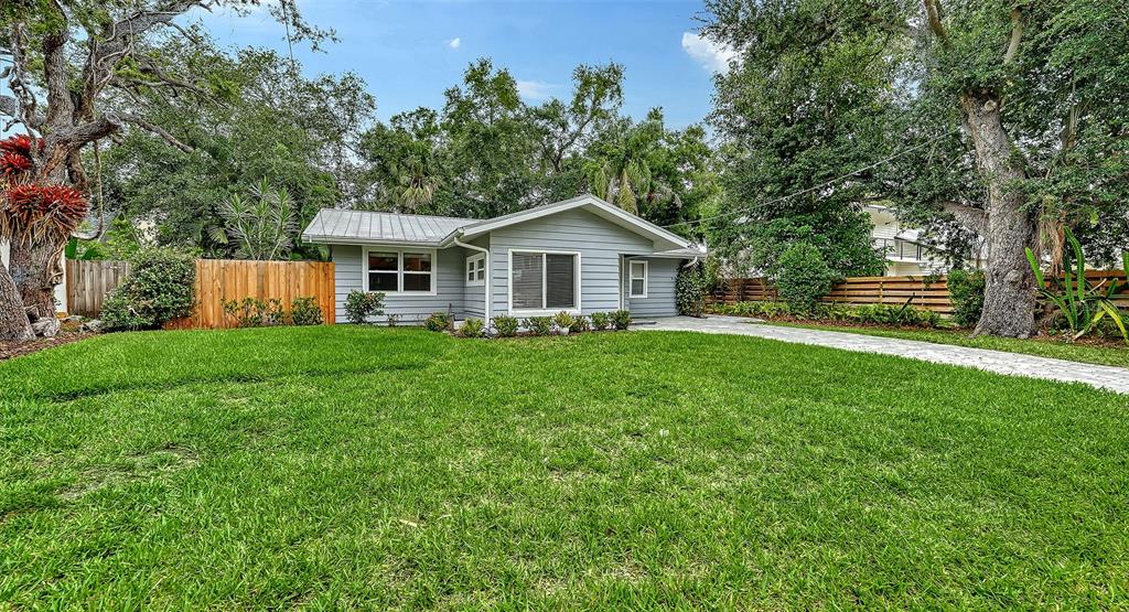 A single-story gray house with a metal roof sits behind a large green lawn — 1773 HARMONY LANE, SARASOTA, FL