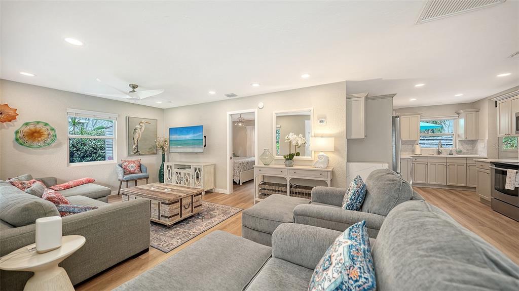 A living room with gray furniture, wood-look flooring, and an open kitchen in the background — 1773 HARMONY LANE, SARASOTA, FL