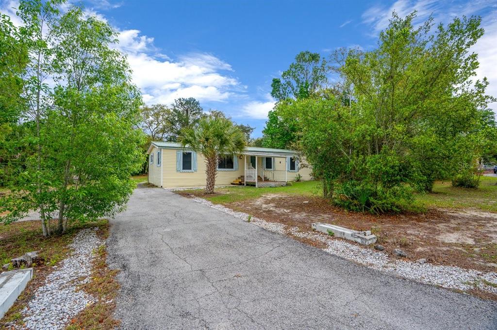 A yellow single-story house with a paved driveway and surrounding trees under a blue sky — 5415 S DOYLE TERRACE, HOMOSASSA, FL