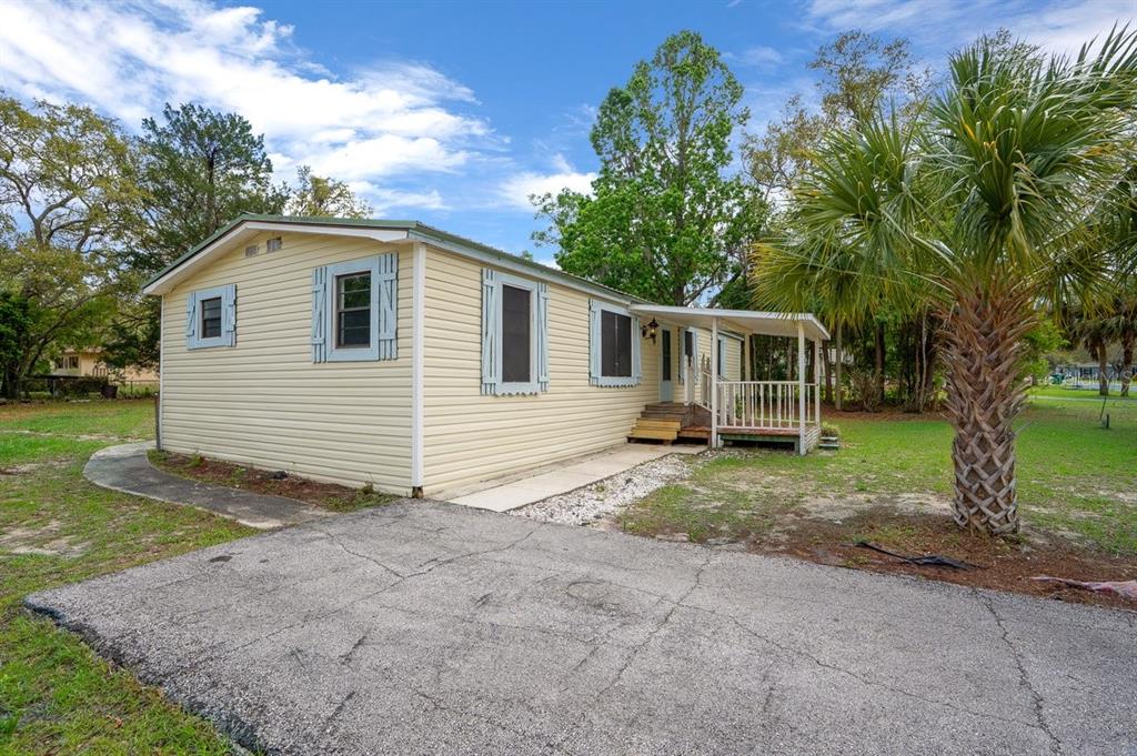 A single-story mobile home with light yellow siding, blue shutters, and a small front porch — 5415 S DOYLE TERRACE, HOMOSASSA, FL