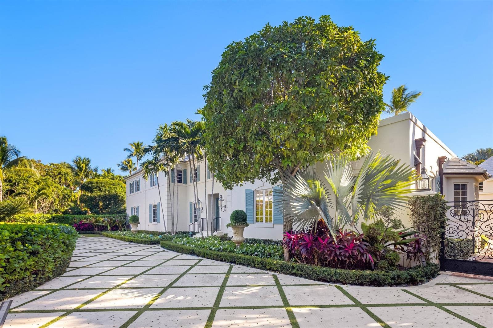 A white two-story house with blue shutters sits behind a paved driveway and lush landscaping — 9 Via Vizcaya, Palm Beach FL 33480, PALM BEACH, FL