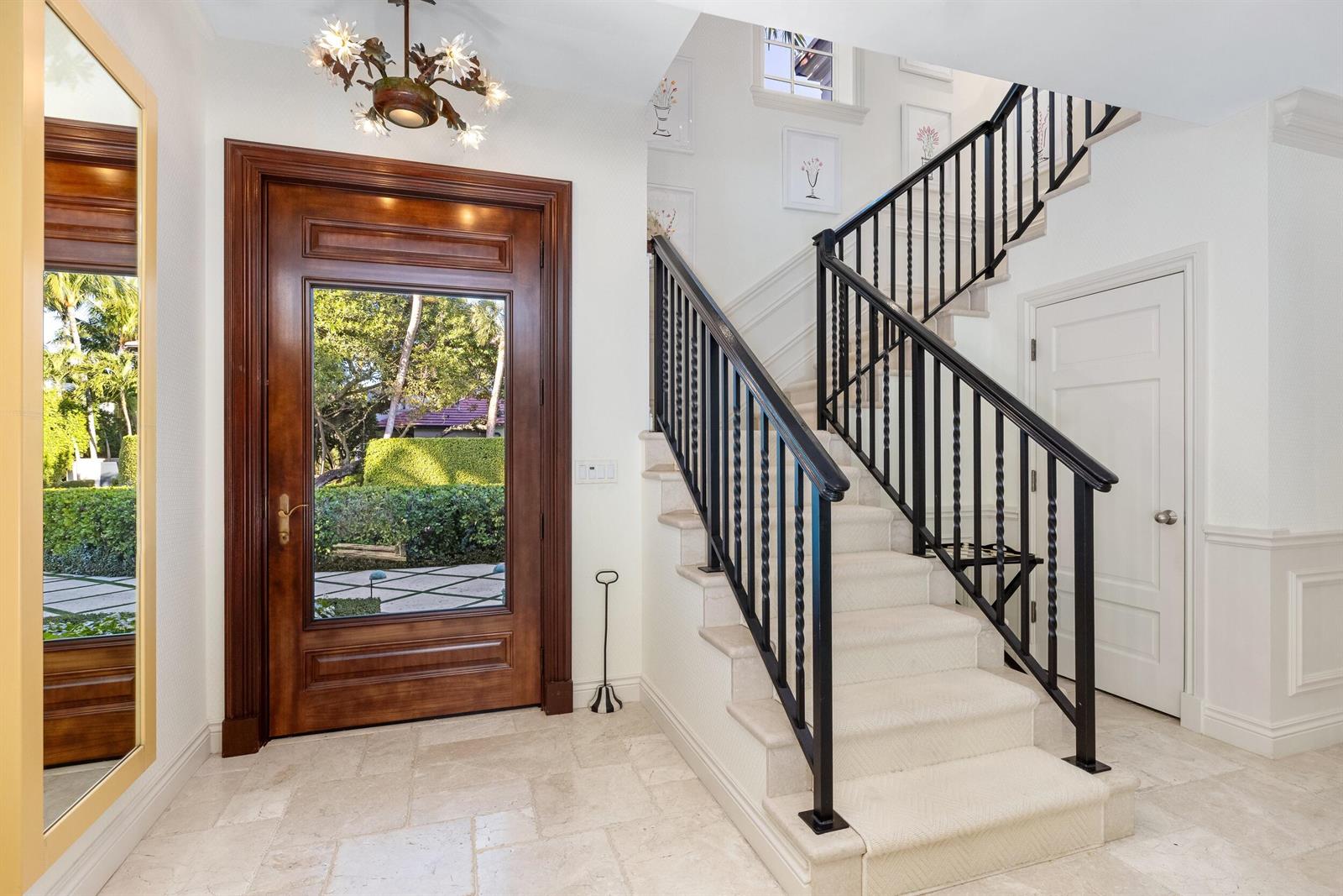 A foyer features a wooden front door, a carpeted staircase with black railings, and tile flooring — 9 Via Vizcaya, Palm Beach FL 33480, PALM BEACH, FL
