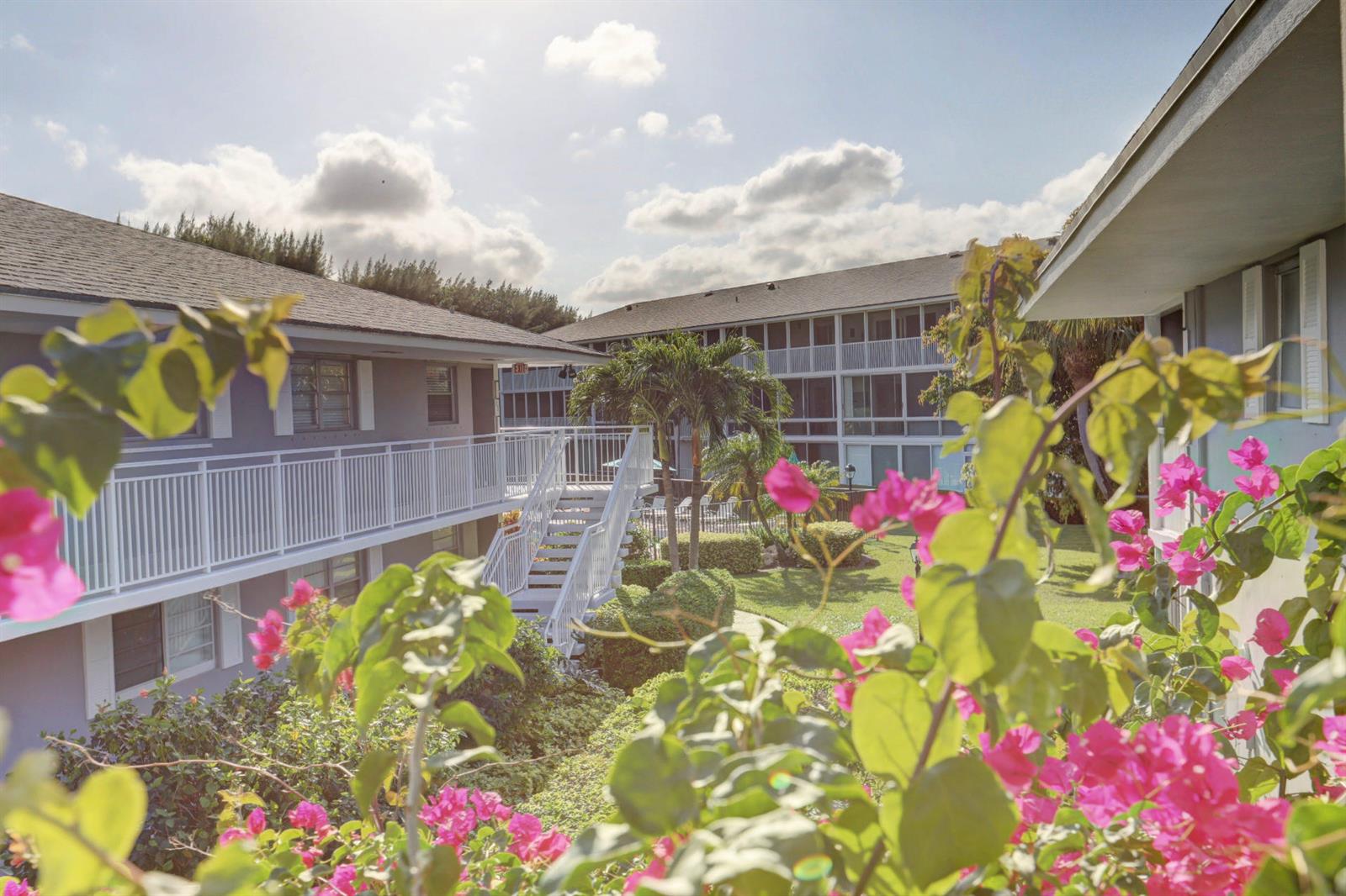 Exterior view of a multi-story apartment complex with white railings, stairs, and pink bougainvillea flowers — 50 Celestial Way # 8e, Juno Beach FL 33408, JUNO BEACH, FL