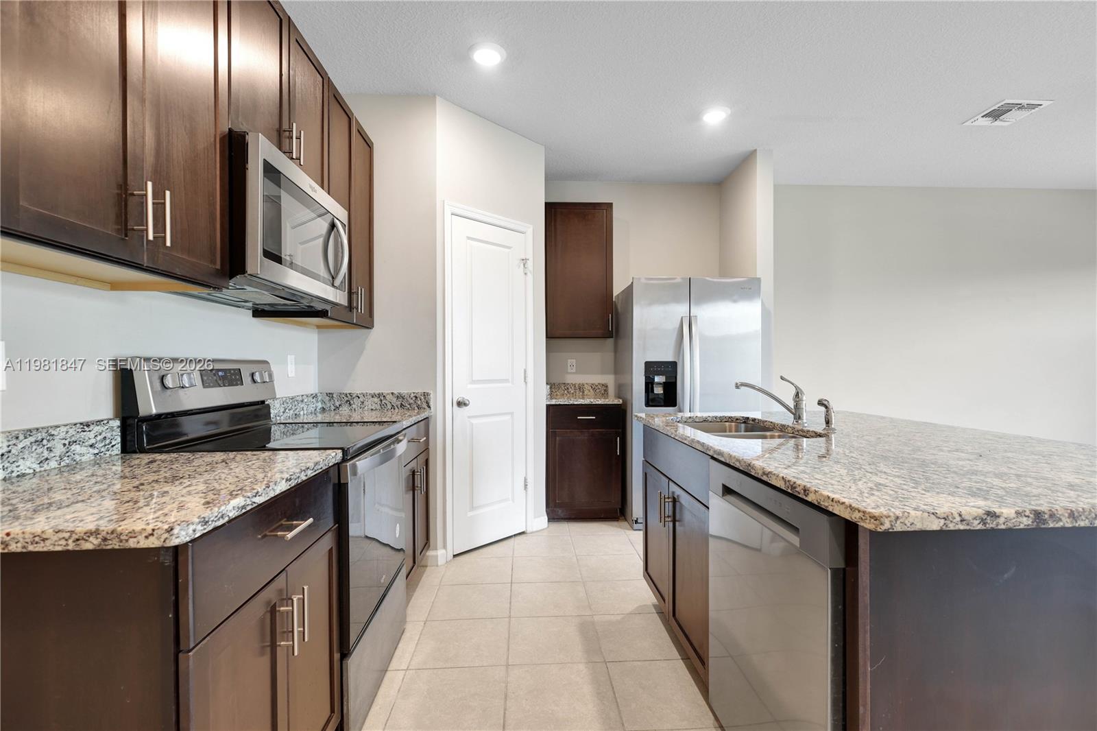 A kitchen features dark wood cabinets, granite countertops, stainless steel appliances, and tile flooring — 1761 Lindley St, Mangonia Park FL 33407, MANGONIA PARK, FL