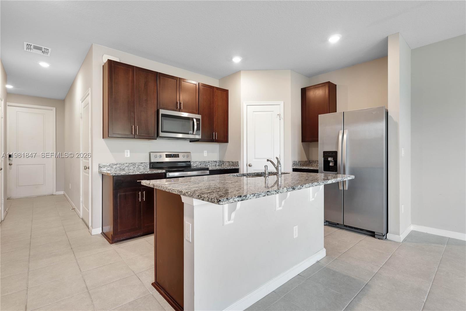 A kitchen features dark wood cabinets, granite countertops, stainless steel appliances, and a central island — 1761 Lindley St, Mangonia Park FL 33407, MANGONIA PARK, FL