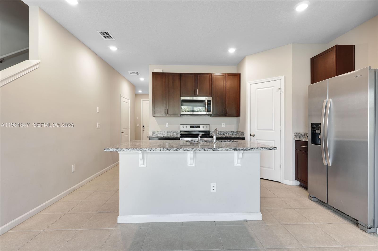 A kitchen features dark wood cabinets, granite countertops, a central island, and stainless steel appliances — 1761 Lindley St, Mangonia Park FL 33407, MANGONIA PARK, FL