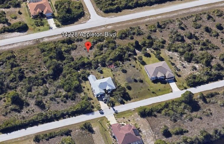 This aerial view shows a vacant lot situated between two houses on a paved road — 14228 APPLETON BOULEVARD, PORT CHARLOTTE, FL