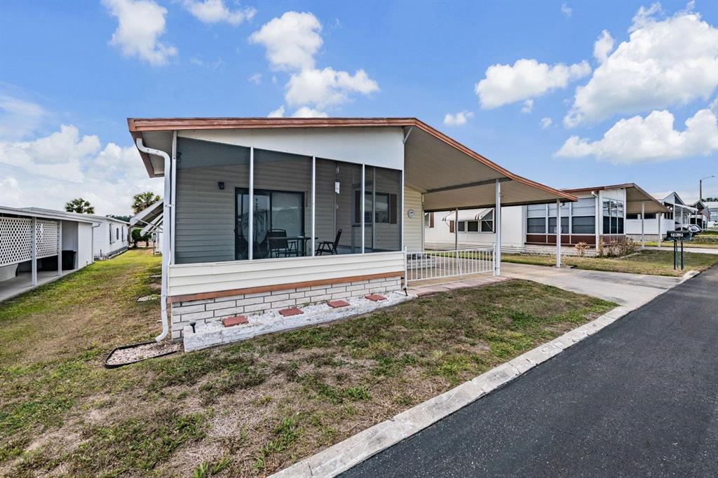 A mobile home features a screened-in porch, a carport, and a brick-accented foundation — 7047 EL MATADOR STREET, ZEPHYRHILLS, FL