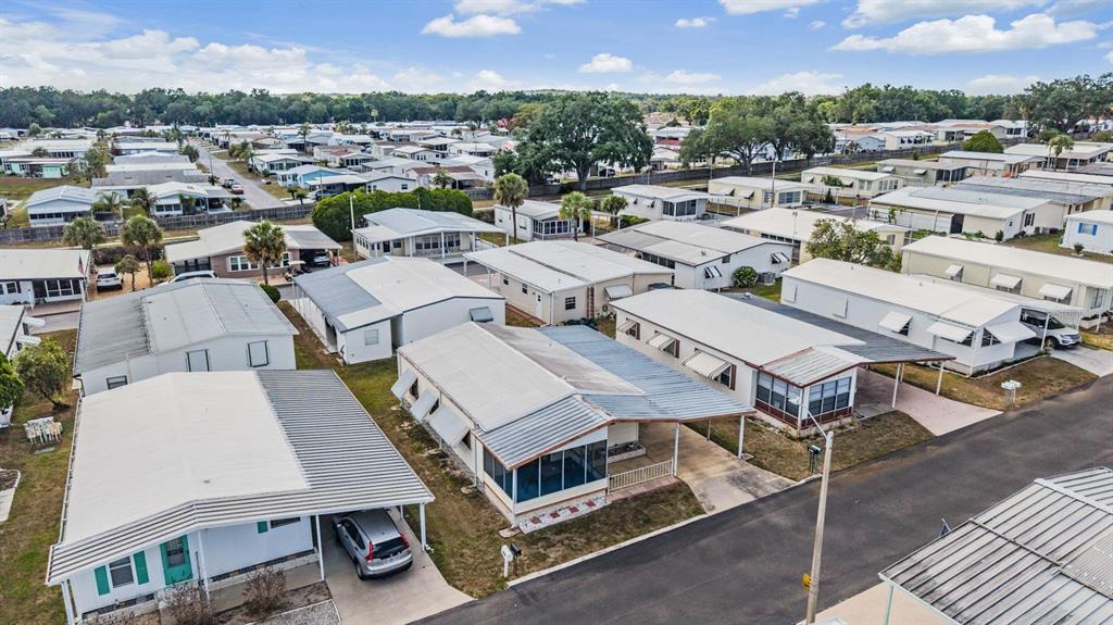 An aerial view shows a dense neighborhood of manufactured homes with metal roofs and carports — 7047 EL MATADOR STREET, ZEPHYRHILLS, FL
