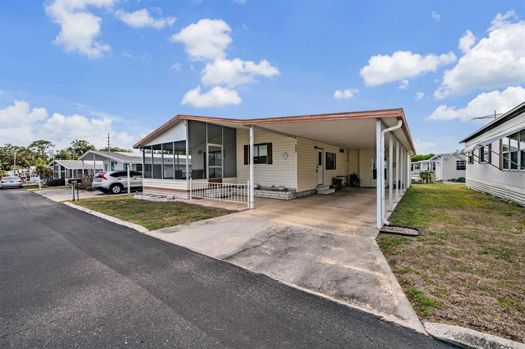 A single-story mobile home with a screened porch, carport, and light-colored siding under a blue sky — 7047 EL MATADOR STREET, ZEPHYRHILLS, FL