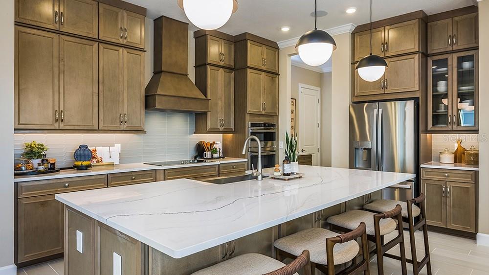 A modern kitchen features wood cabinets, a large white quartz island, and stainless steel appliances — 26752 DOVE DRIVE, PUNTA GORDA, FL