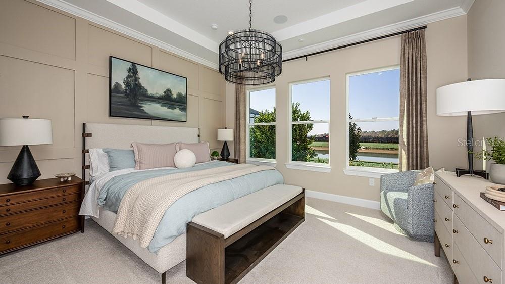 A bedroom features a paneled accent wall, a chandelier, and windows overlooking a pond — 26752 DOVE DRIVE, PUNTA GORDA, FL