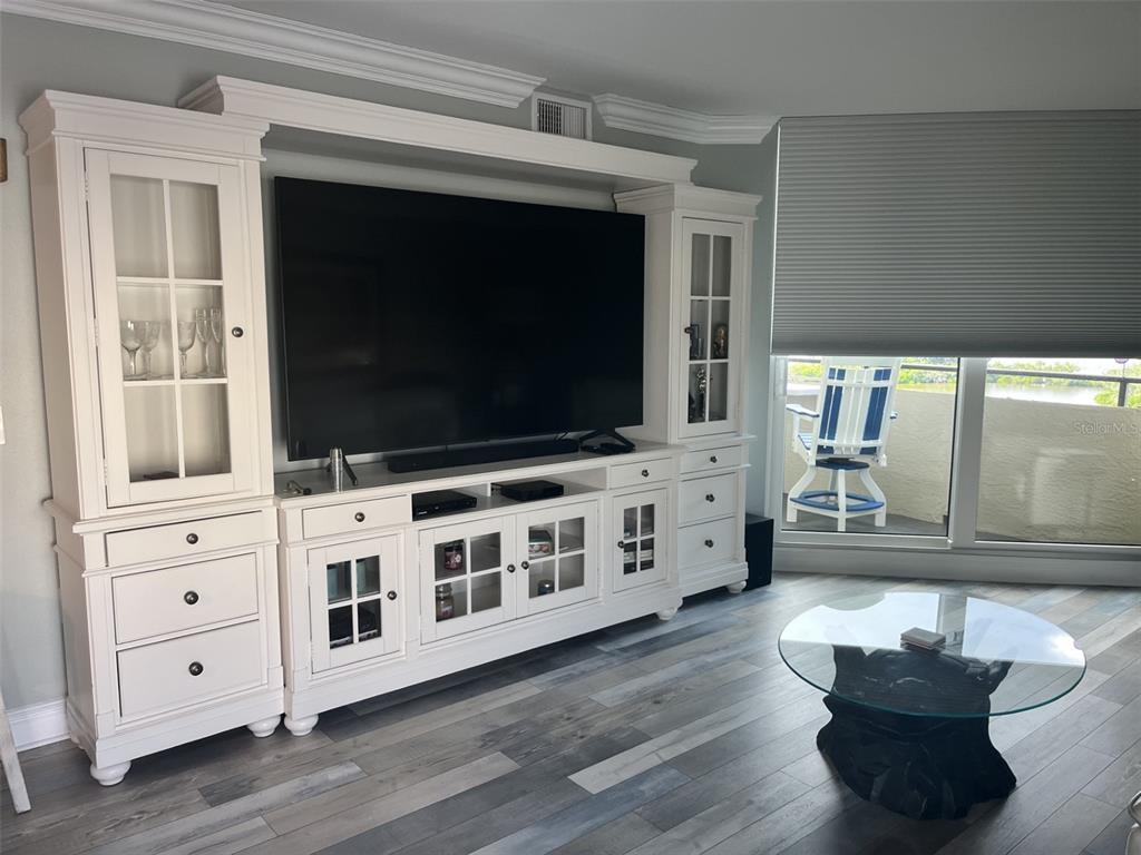 A living room features a large white entertainment center, wood-look flooring, and a glass-topped table — 5915 SEA RANCH DRIVE UNIT 703, HUDSON, FL