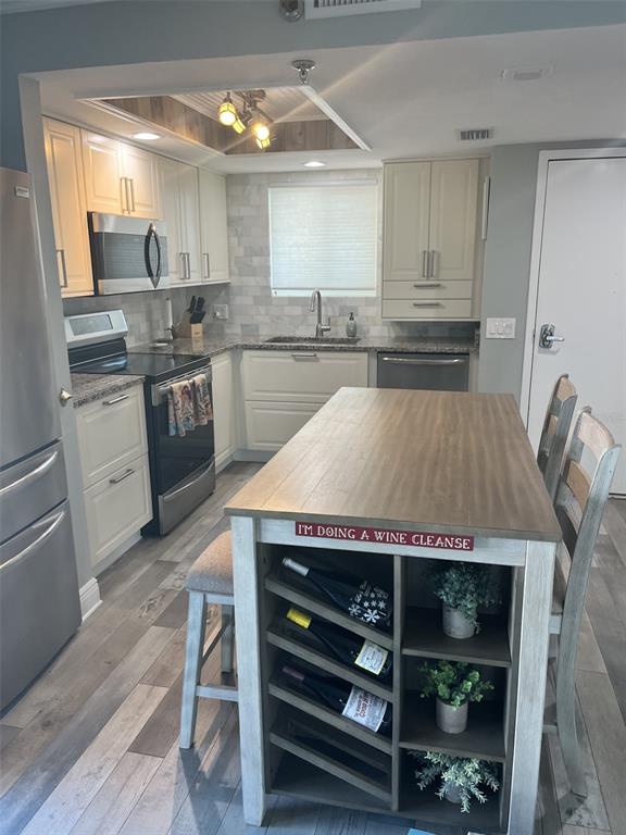 A kitchen with light cabinets, stainless steel appliances, a kitchen island, and wood-look flooring — 5915 SEA RANCH DRIVE UNIT 703, HUDSON, FL