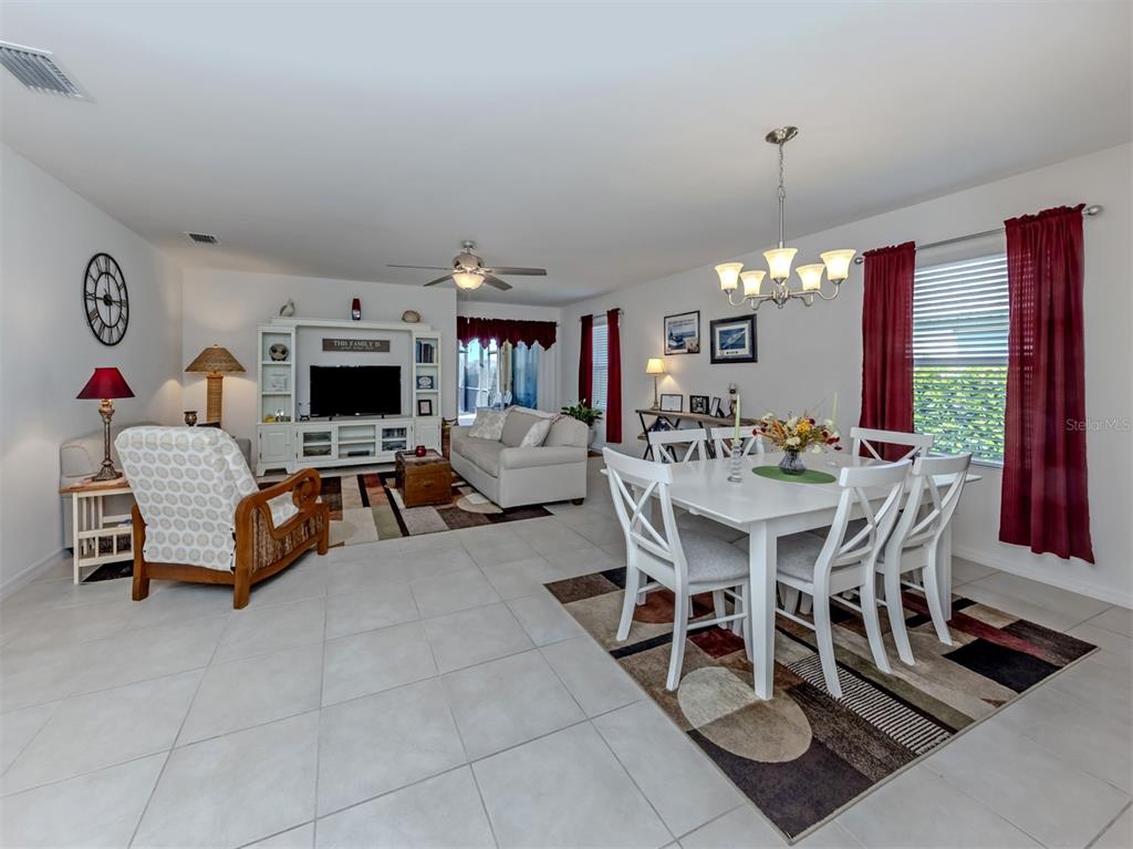 An open-concept living and dining area features white tile flooring, a chandelier, and red curtains — 7045 WATERFORD PARKWAY, PUNTA GORDA, FL