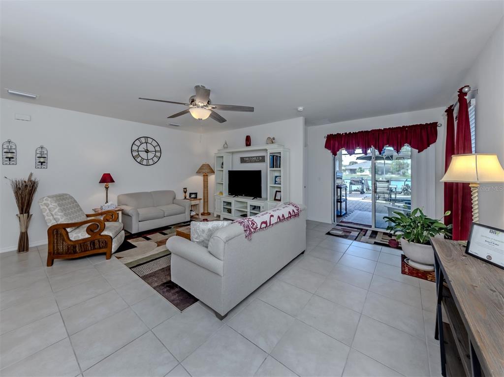 A bright living room features tile flooring, a ceiling fan, and sliding doors to a patio — 7045 WATERFORD PARKWAY, PUNTA GORDA, FL