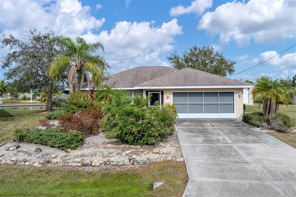A single-story house with a concrete driveway, a screened garage door, and landscaped front yard — 15500 LONGVIEW ROAD, PORT CHARLOTTE, FL