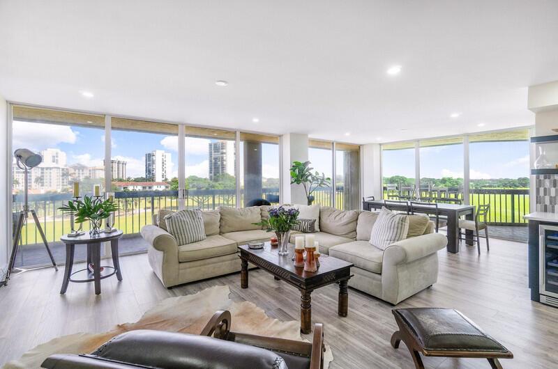 A bright living room features a large sectional sofa, wood coffee table, and floor-to-ceiling windows — 1900 Consulate Place # 406, West Palm Beach FL 33401, WEST PALM BEACH, FL
