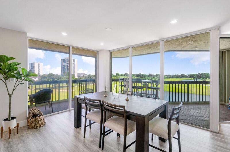 A dining area features a wooden table, four chairs, and floor-to-ceiling windows overlooking a golf course — 1900 Consulate Place # 406, West Palm Beach FL 33401, WEST PALM BEACH, FL