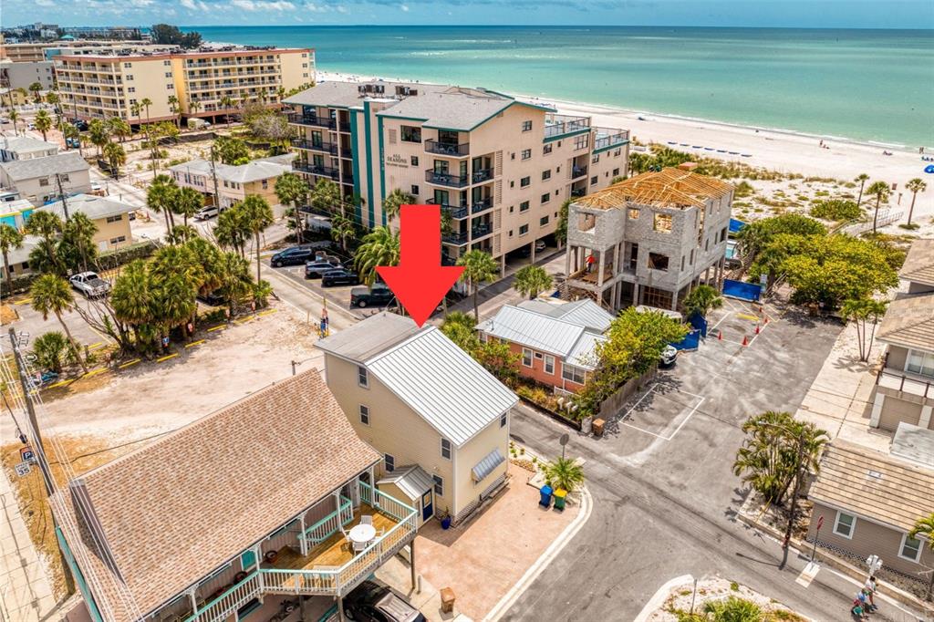 An aerial view shows a yellow multi-story house with a metal roof near the beach — 13095 GULF LANE, MADEIRA BEACH, FL
