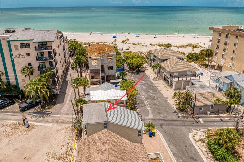 An aerial view shows a tan house with a metal roof near a sandy beach — 13095 GULF LANE, MADEIRA BEACH, FL