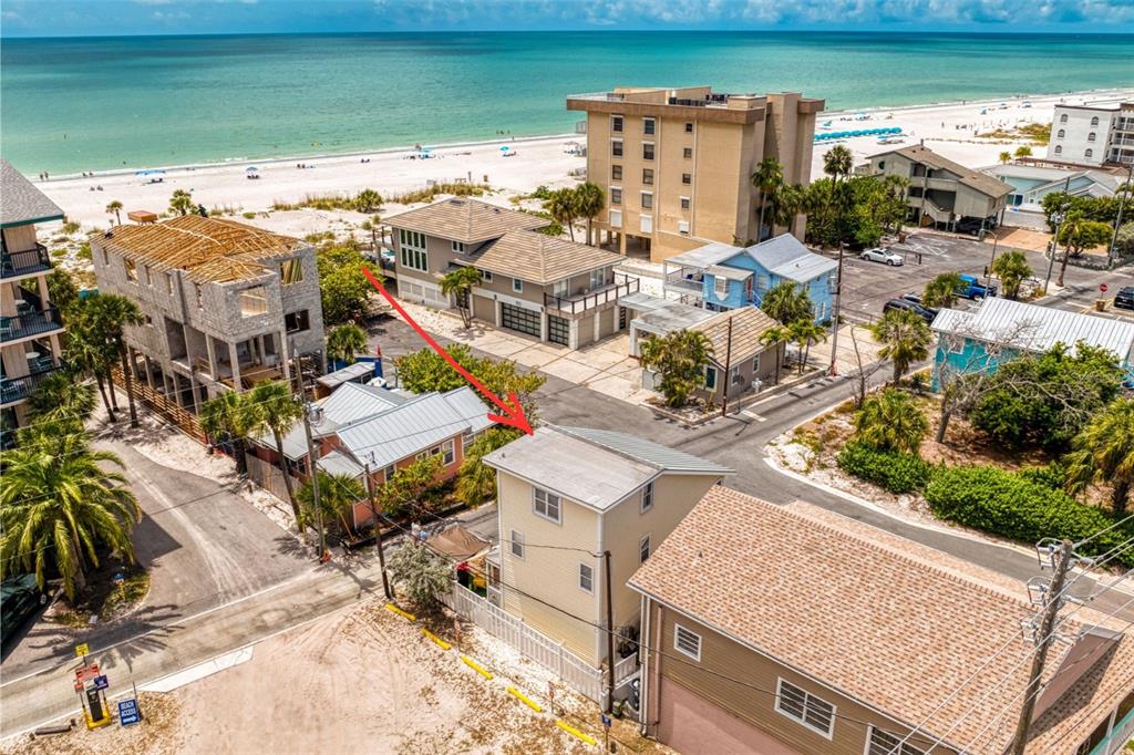 An aerial view shows a yellow multi-story house near a beach with other nearby buildings — 13095 GULF LANE, MADEIRA BEACH, FL