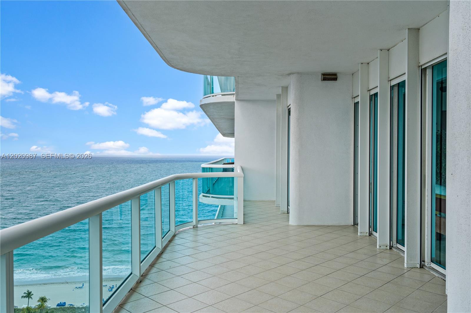 A tiled balcony overlooks the ocean with glass railings and floor-to-ceiling sliding glass doors — 10101 Collins Ave, Bal Harbour FL 33154, BAL HARBOUR, FL