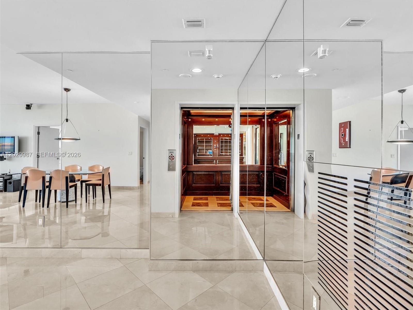 A dining area with a private elevator entrance featuring wood paneling and mirrored walls — 10101 Collins Ave, Bal Harbour FL 33154, BAL HARBOUR, FL