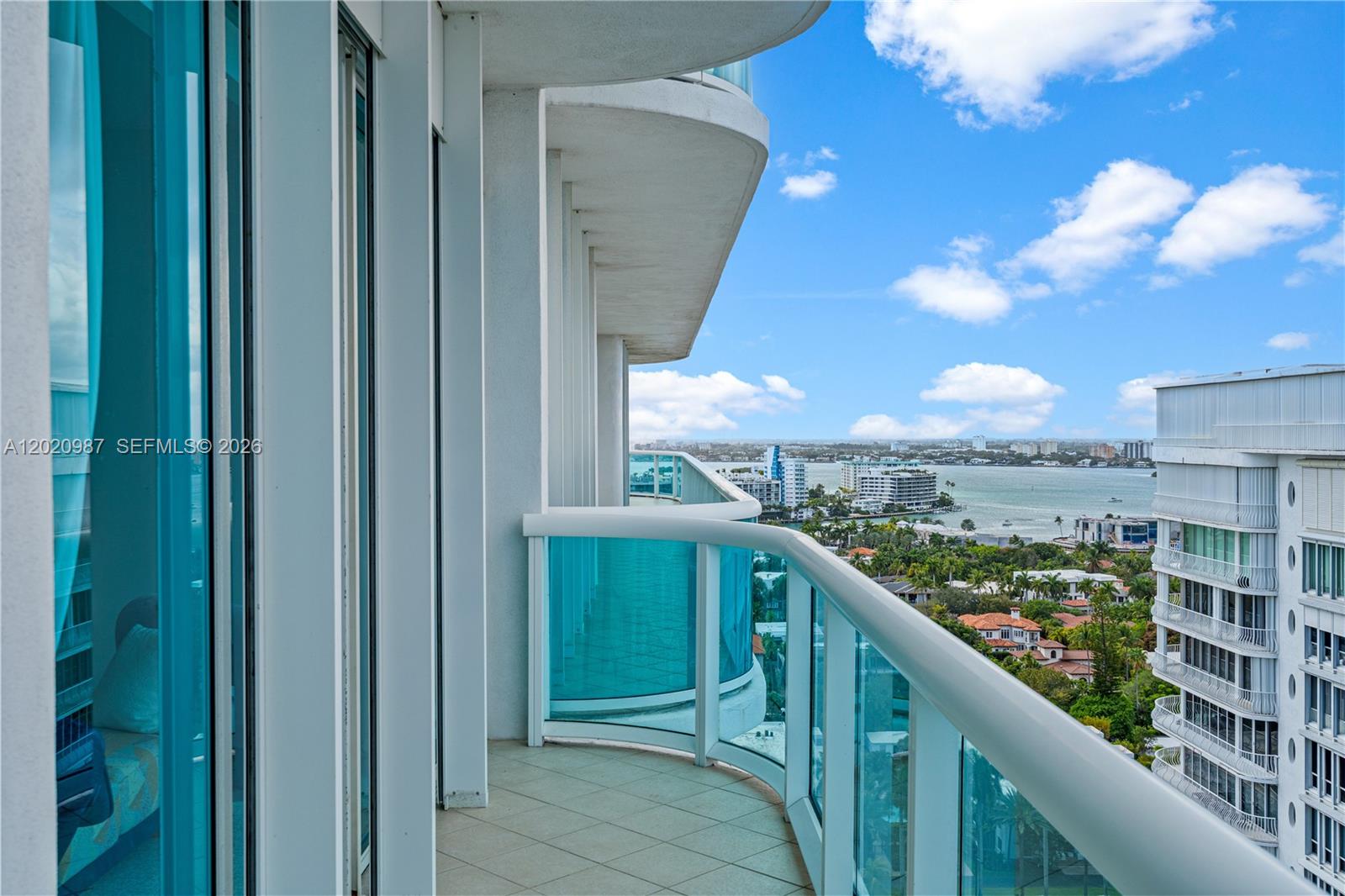 A curved balcony with glass railings overlooks a coastal city and a body of water — 10101 Collins Ave, Bal Harbour FL 33154, BAL HARBOUR, FL