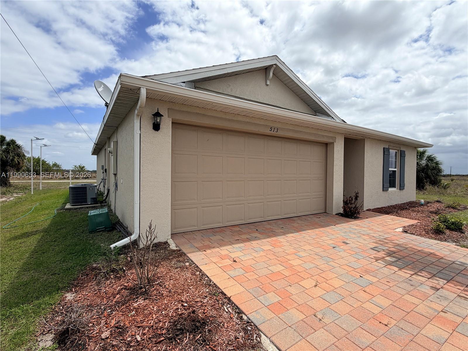 A tan stucco house features a two-car garage and a brick paver driveway — 513 Ella Jean PL, La Belle FL 33935, LA BELLE, FL