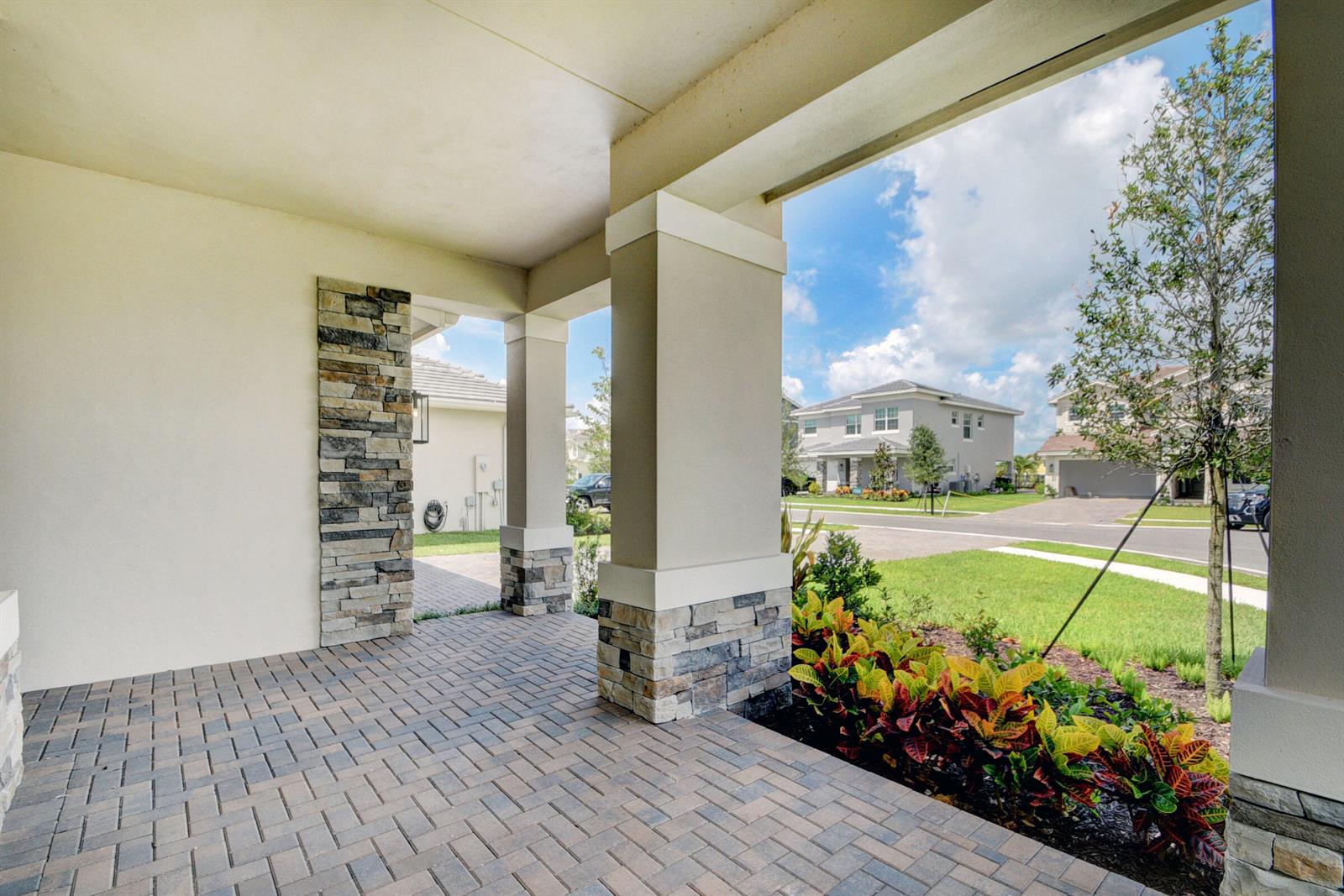 A covered porch features stone-accented columns, brick paver flooring, and a view of the street — 1366 Harvester Crossing, FL 33470, FL