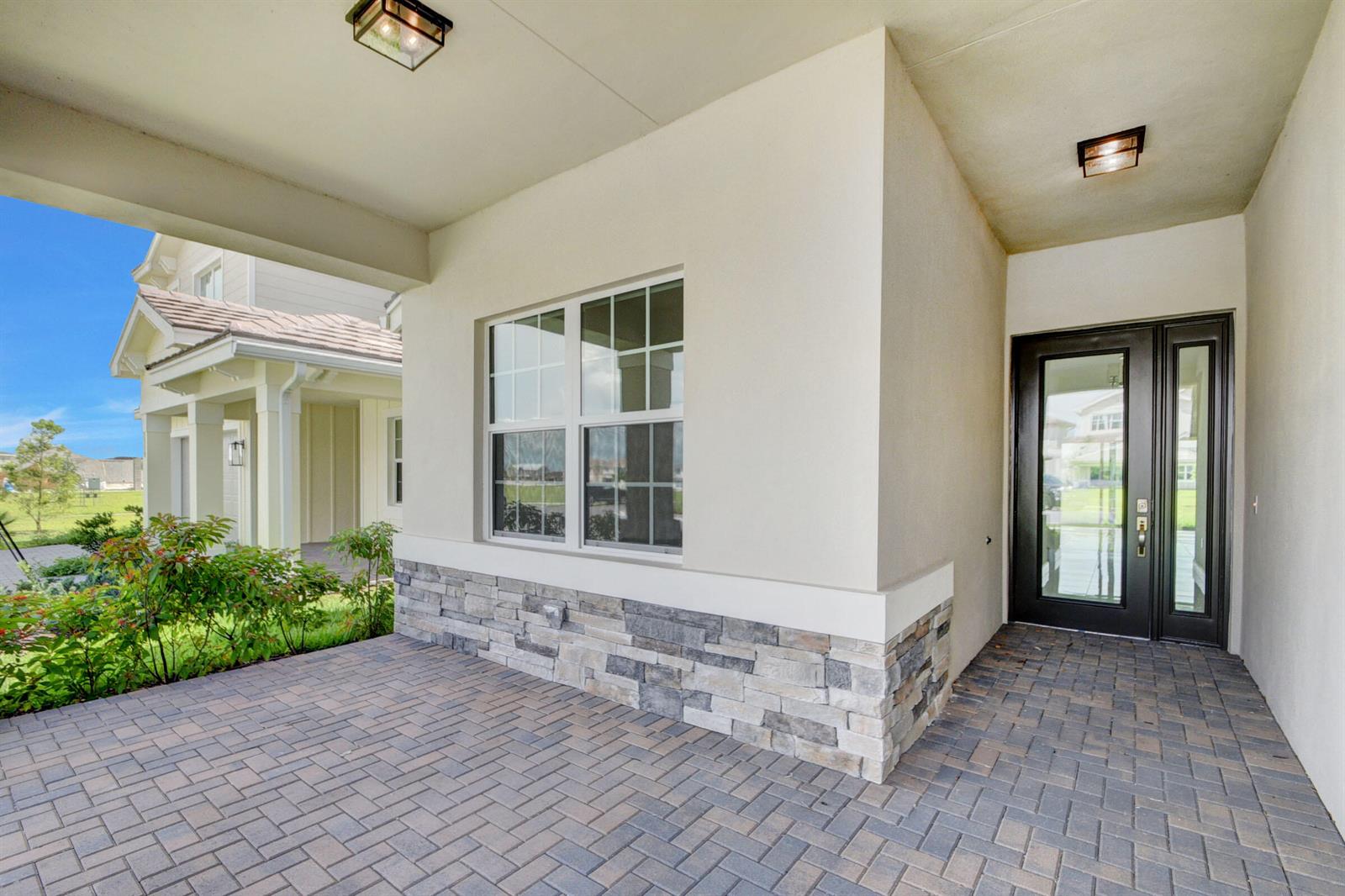 A covered front porch features stone veneer, brick pavers, and a dark glass-paneled front door — 1366 Harvester Crossing, FL 33470, FL