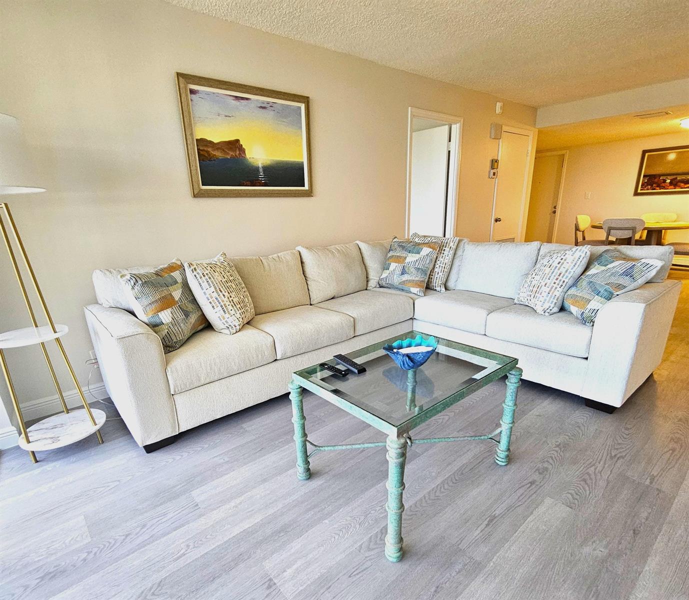 A living room features a beige sectional sofa, a glass coffee table, and light flooring — 1357 NE Ocean Boulevard # 215, Stuart FL 34996, STUART, FL