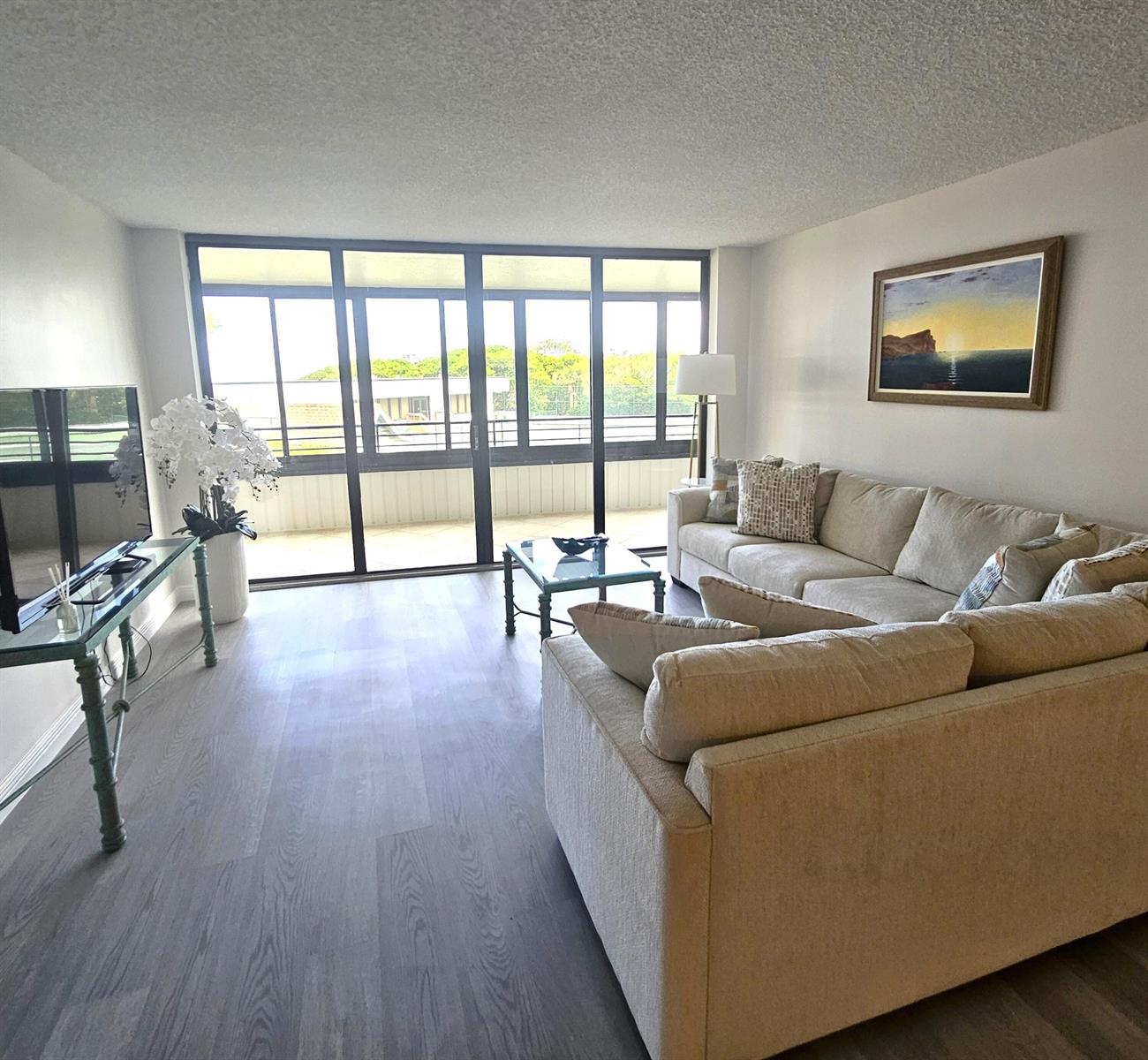 A living room features a beige sectional sofa, glass coffee table, and large sliding glass doors — 1357 NE Ocean Boulevard # 215, Stuart FL 34996, STUART, FL