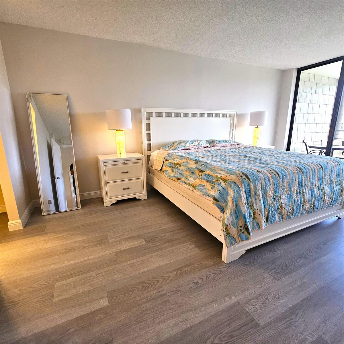 A bedroom with a white bed frame, two nightstands, lamps, a floor mirror, and balcony — 1357 NE Ocean Boulevard # 215, Stuart FL 34996, STUART, FL