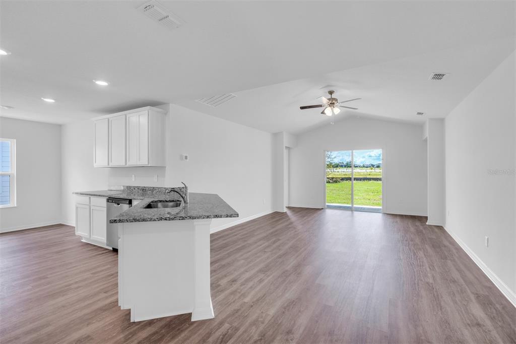 An open-concept kitchen and living area featuring white cabinets, granite countertops, and wood-look flooring — 40 PRESIDENTIAL LANE, PALM COAST, FL