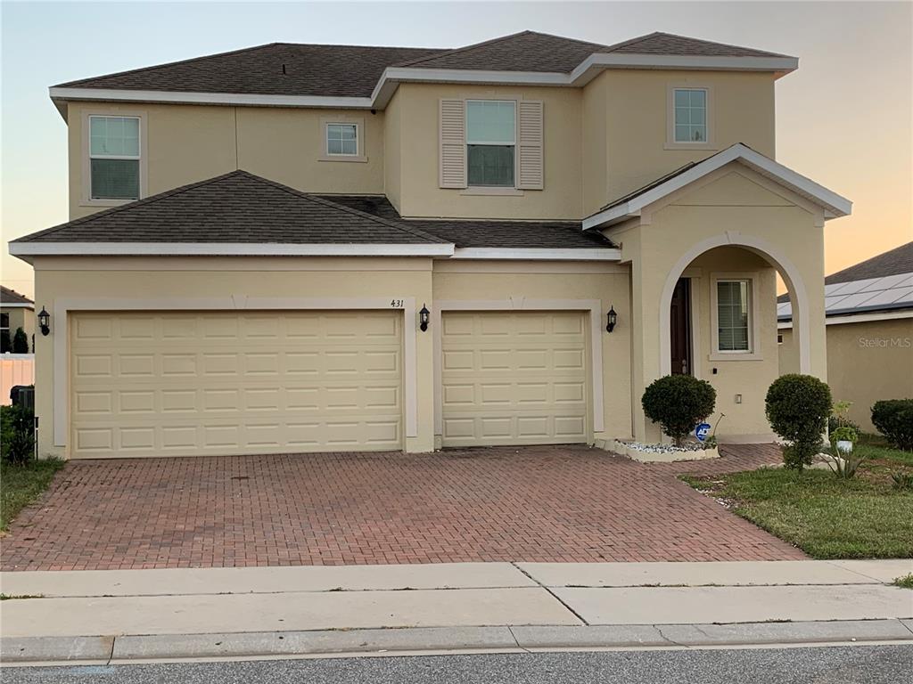 A two-story house with a tan stucco exterior, a brick driveway, and a three-car garage — 431 ARAGOSA DRIVE, DAVENPORT, FL