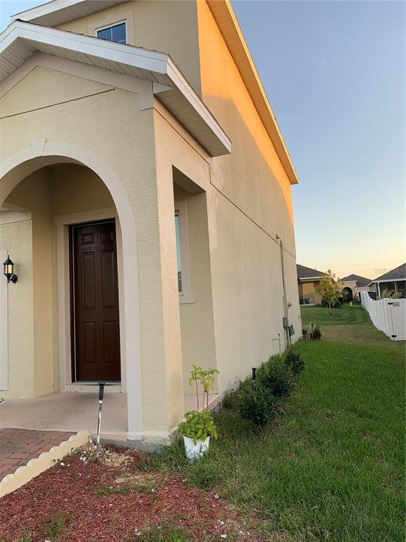 A side view of a beige house exterior featuring a covered entryway and a small lawn — 431 ARAGOSA DRIVE, DAVENPORT, FL