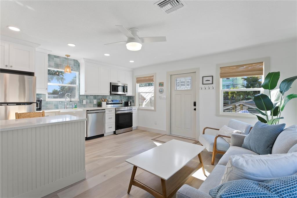A bright open-concept kitchen and living area with white cabinets, stainless appliances, and wood flooring — 800 GULF BOULEVARD UNIT 5, INDIAN ROCKS BEACH, FL