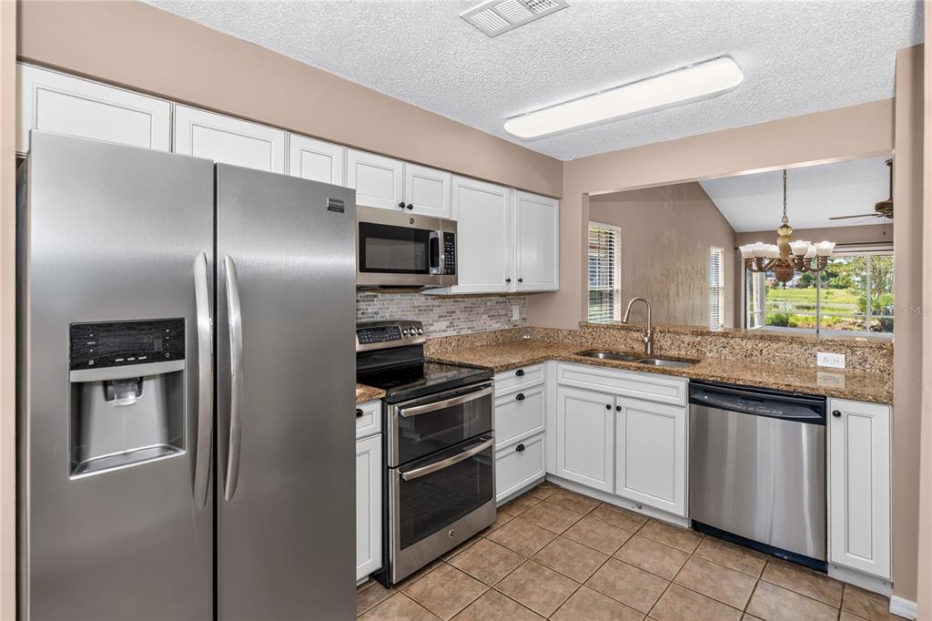 A kitchen with white cabinets, granite countertops, stainless steel appliances, and a pass-through window — 168 BERMUDA PETREL COURT, DAYTONA BEACH, FL