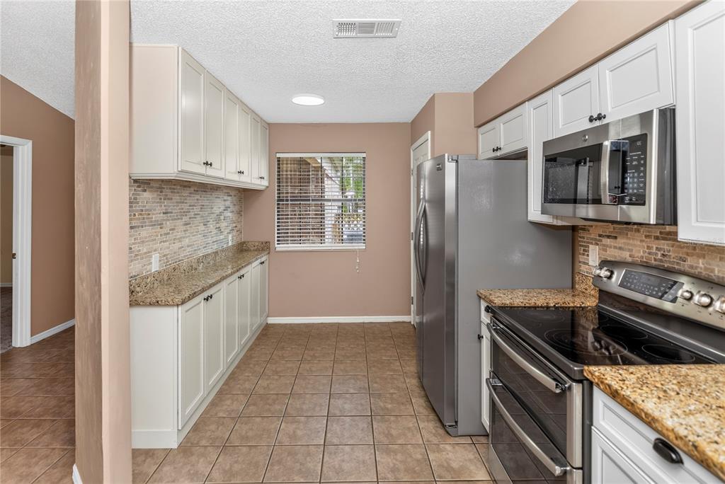 A kitchen features light cabinets, granite countertops, stainless steel appliances, and tile flooring — 168 BERMUDA PETREL COURT, DAYTONA BEACH, FL