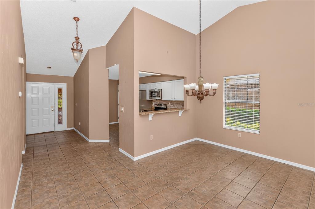 A dining area with tile floors, a chandelier, and a pass-through window to the kitchen — 168 BERMUDA PETREL COURT, DAYTONA BEACH, FL
