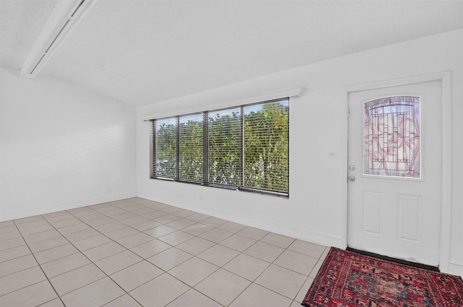 An empty room with white walls, light-colored tile flooring, a large window, and a front door — 424 NW 12th Avenue, Boca Raton FL 33486, BOCA RATON, FL
