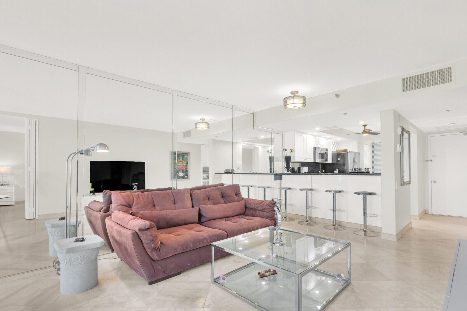 A living room with a purple sofa, glass coffee table, and a mirrored wall — 2687 N Ocean Boulevard # 306, Boca Raton FL 33431, BOCA RATON, FL