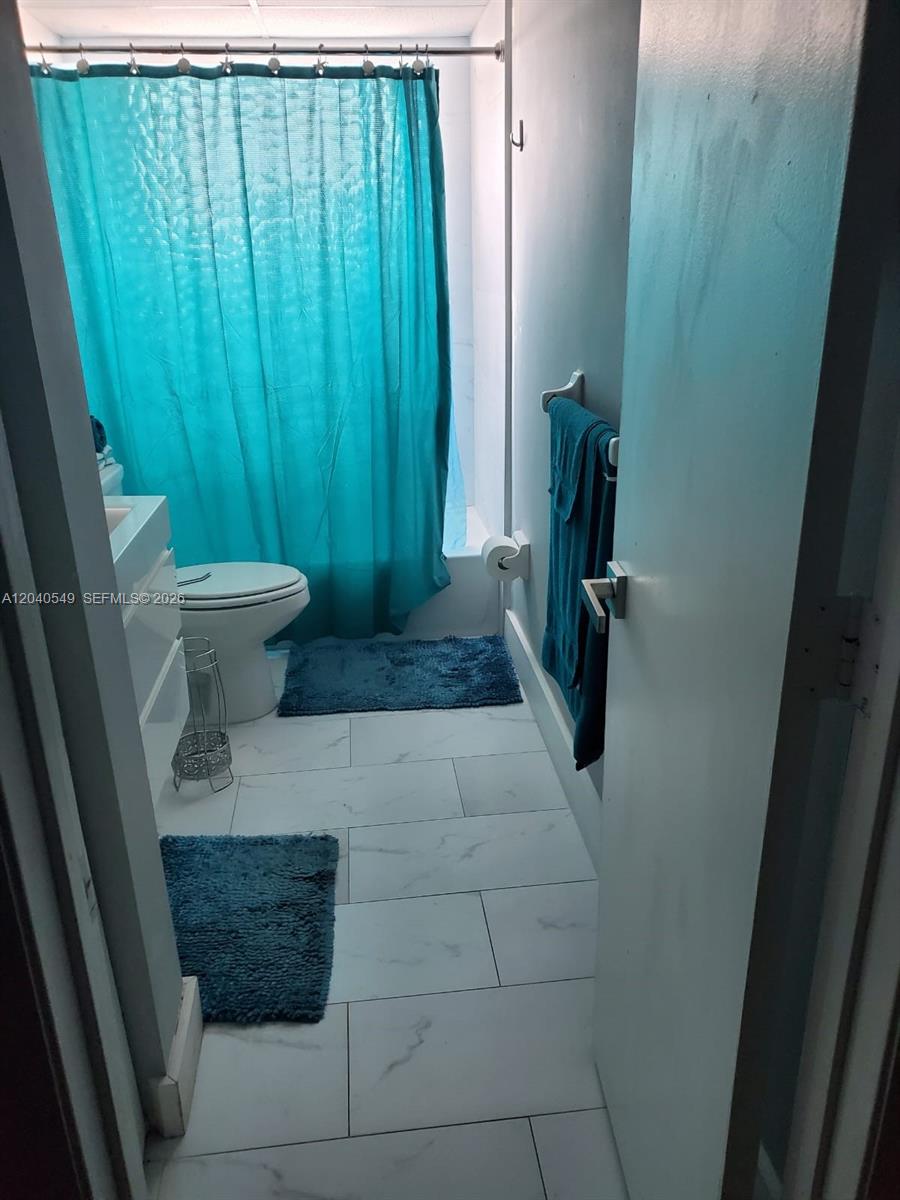 A bathroom features white tile flooring, a toilet, and a teal shower curtain — 140 NW 87th Ave # G214, Miami FL 33172, MIAMI, FL