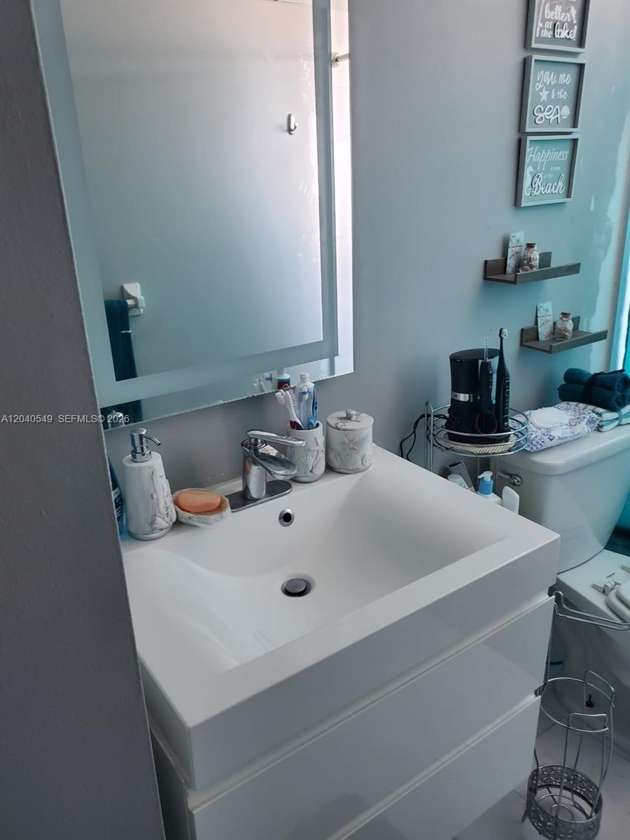 A bathroom features a white vanity, a rectangular mirror, and wall-mounted decor above the toilet — 140 NW 87th Ave # G214, Miami FL 33172, MIAMI, FL