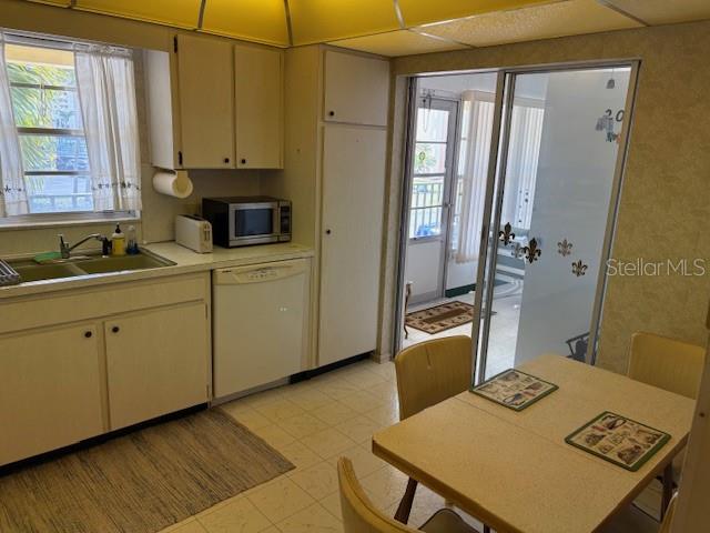 A kitchen with white cabinets, a dishwasher, and a dining table next to a patio — 4700 COVE CIRCLE UNIT 203, ST PETERSBURG, FL